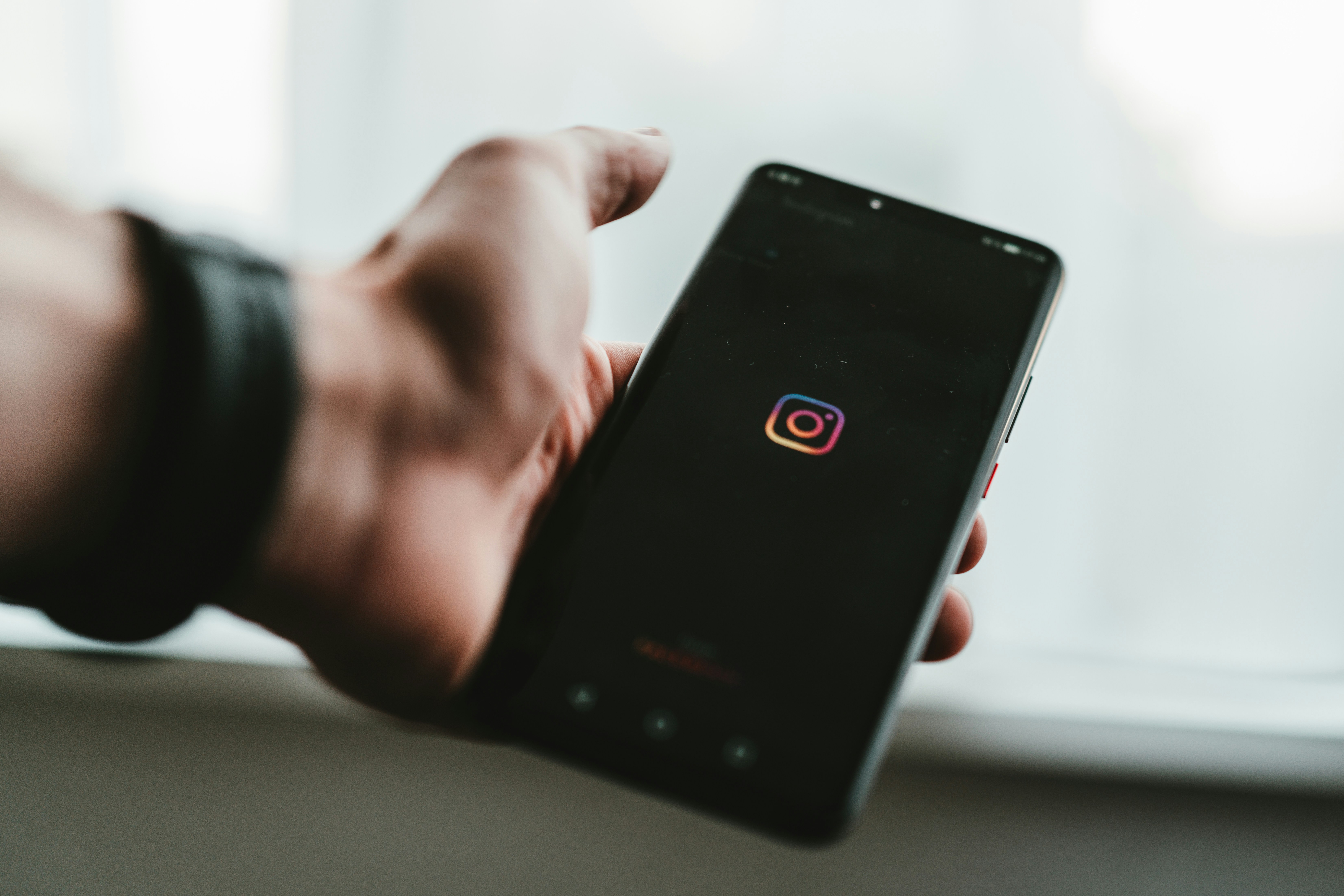 A hand holding a phone with the Instagram logo shown on the screen.